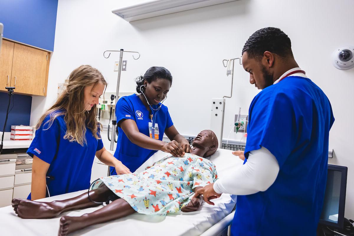 Three Shenandoah University nursing students simulating care by working with a manikin.